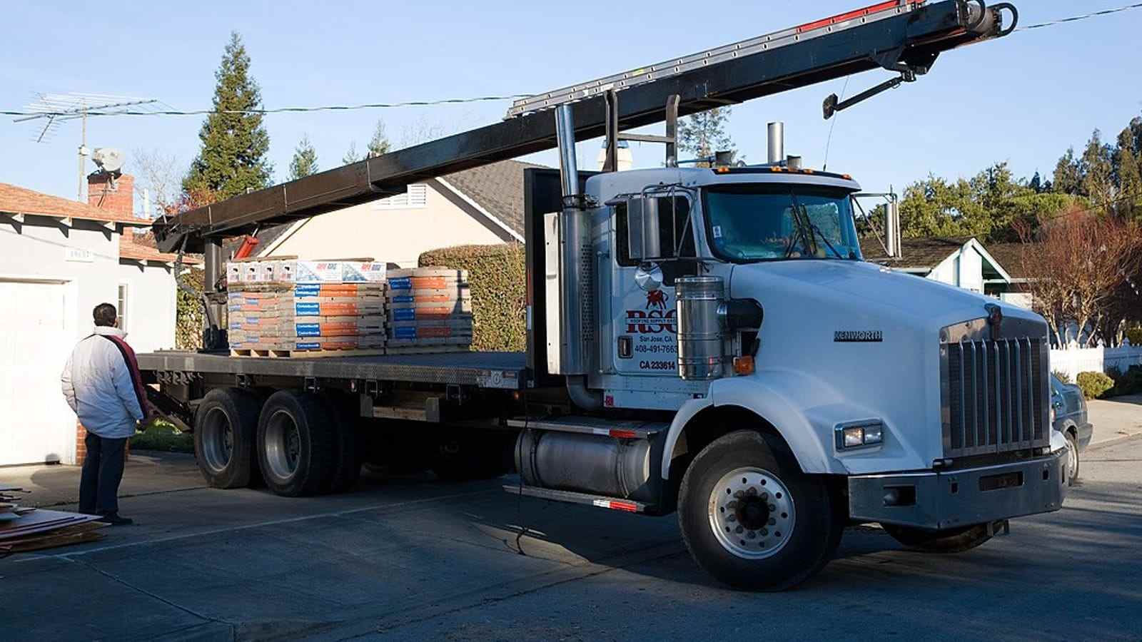 A boom truck unloading banded roofing shingles onto a driveway